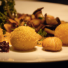 Drei panierte Dauphine-Kartoffeln auf weißem Teller mit sautierten Pilzen, Kräutern und dunklem Chutney