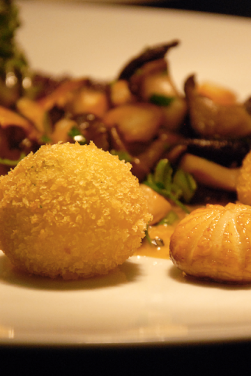 Drei panierte Dauphine-Kartoffeln auf weißem Teller mit sautierten Pilzen, Kräutern und dunklem Chutney