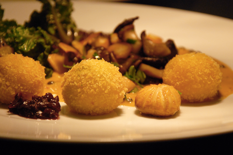 Drei panierte Dauphine-Kartoffeln auf weißem Teller mit sautierten Pilzen, Kräutern und dunklem Chutney