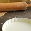 Quiche-Teig in weißer Tarteform, Nudelholz und Zitrone auf bemehlter Arbeitsfläche