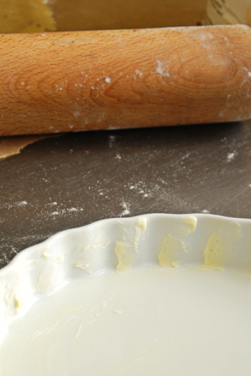 Quiche-Teig in weißer Tarteform, Nudelholz und Zitrone auf bemehlter Arbeitsfläche