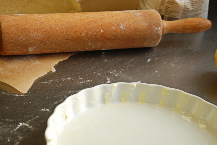 Quiche-Teig in weißer Tarteform, Nudelholz und Zitrone auf bemehlter Arbeitsfläche