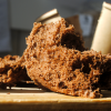 Aufgeschnittener Schokoladen-Sponge mit luftig-poröser Krume auf Holzbrett, im Hintergrund Coffee-to-go-Becher