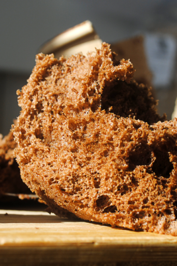 Aufgeschnittener Schokoladen-Sponge mit luftig-poröser Krume auf Holzbrett, im Hintergrund Coffee-to-go-Becher