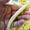 Hand formt einen Schupfnudel-Strang aus gelbem Kartoffelteig, bestäubt mit Mehl