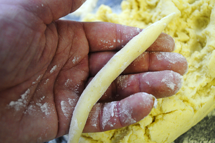 Hand formt einen Schupfnudel-Strang aus gelbem Kartoffelteig, bestäubt mit Mehl