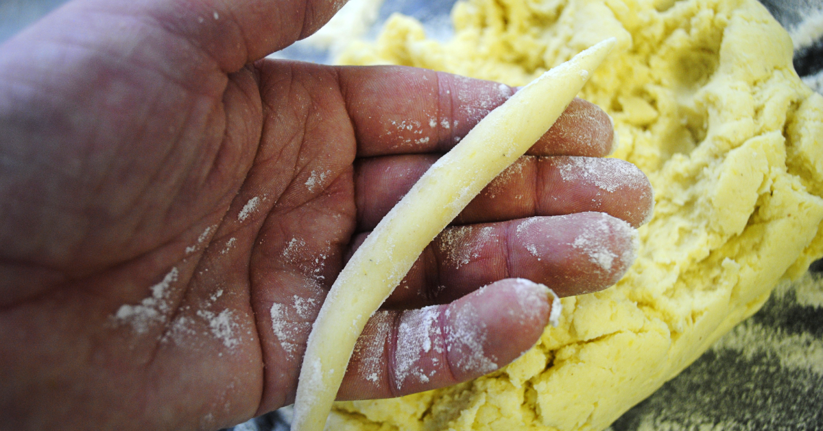 Hand formt einen Schupfnudel-Strang aus gelbem Kartoffelteig, bestäubt mit Mehl
