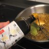 Hand gießt Yamaroku Tsuru Bishio Sojasoße in Pfanne mit Senfkaviar und Lorbeerblatt